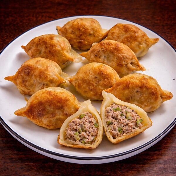 Pan-fried dumplings on a plate, with one cut in half to show the minced meat and green onion filling