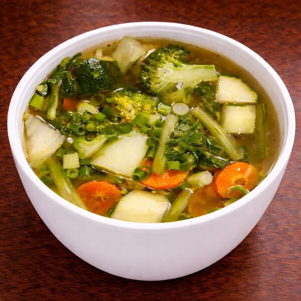 A white bowl filled with vegetable soup containing broccoli, carrots, and zucchini in a clear broth