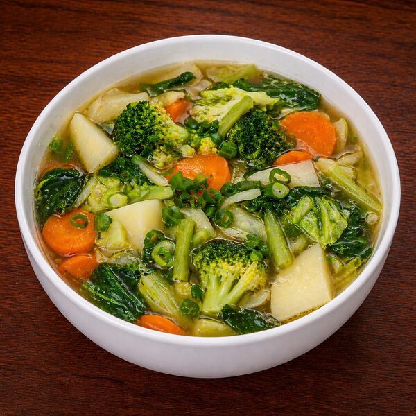 A white bowl filled with vegetable soup containing broccoli, carrots, potatoes, and leafy greens