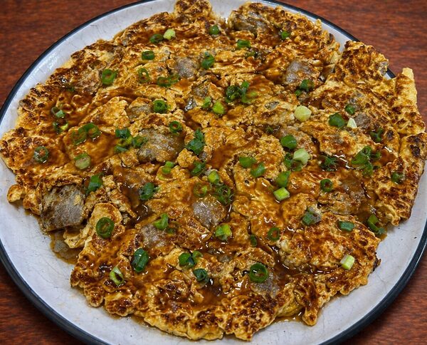 Okonomiyaki pancake topped with savory sauce and chopped green onions
