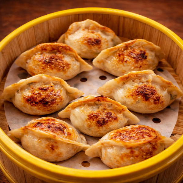 Pan-fried dumplings arranged in a circular bamboo steamer basket