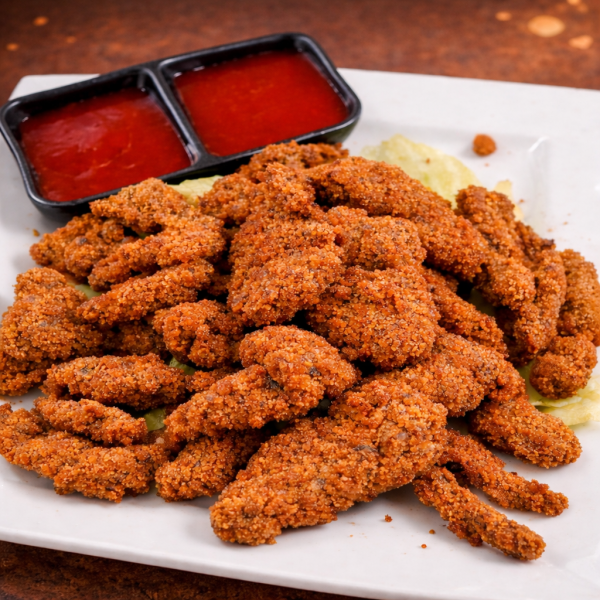 A plate of crispy breaded chicken strips served with a side of red dipping sauce