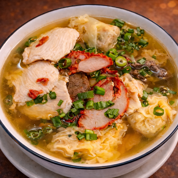 Bowl of wonton soup topped with sliced chicken, red-edged roast pork, and chopped green onions