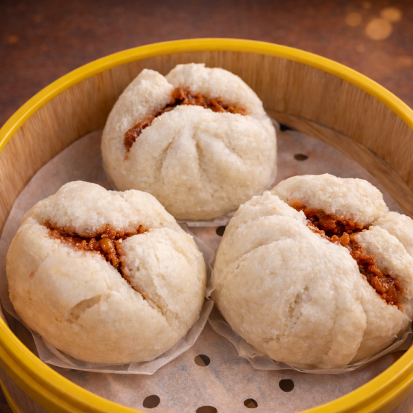 Three steamed char siu bao buns with visible savory pork filling in a bamboo steamer