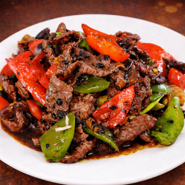 Stir-fried beef with red bell peppers, green peppers, and black beans on a white plate