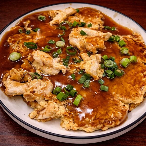 Chicken egg foo young topped with brown gravy and chopped green onions on a white plate