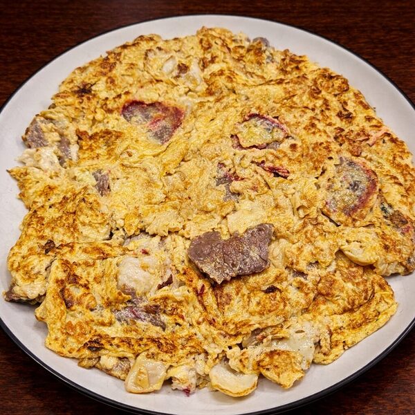 Golden brown omelet cooked with pieces of seared beef and red radish on a white plate