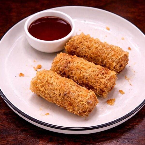 Three crispy, golden-brown fried spring rolls served on a white plate with a side of dipping sauce