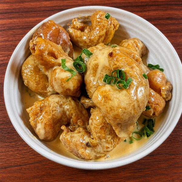 Bowl of crispy fried shrimp coated in a creamy, golden-brown sauce and garnished with chopped green onions