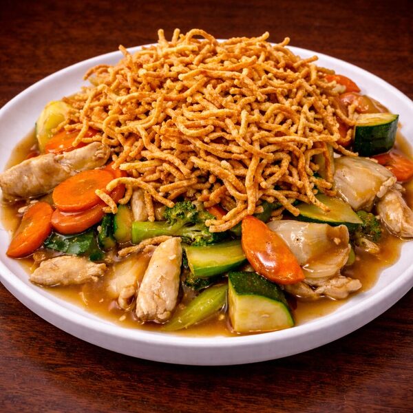 Chicken chow mein with sliced carrots, zucchini, and broccoli topped with crispy fried noodles on a white plate