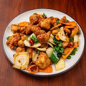 Stir-fried chicken with carrots, onions, green peppers, and dried chili peppers on a white plate