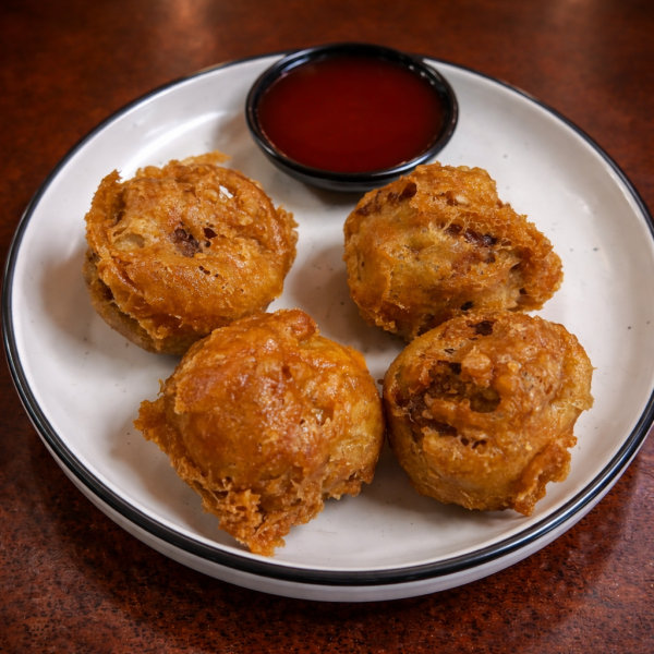 Four golden-brown deep-fried appetizers served on a white plate with a small dish of red dipping sauce