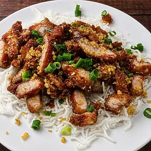 Crispy garlic pork belly served over a bed of thin rice noodles and garnished with chopped green onions