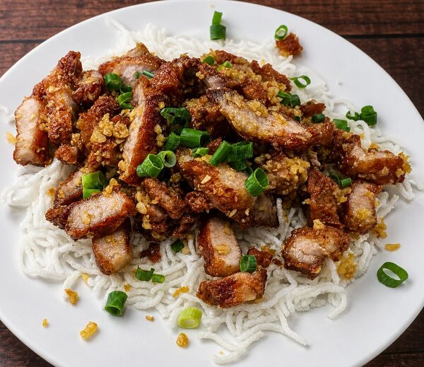 Crispy garlic pork belly served over a bed of thin rice noodles and garnished with chopped green onions
