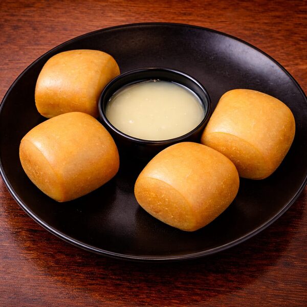 Four golden-brown fried mantou buns served on a black plate with a side of sweetened condensed milk