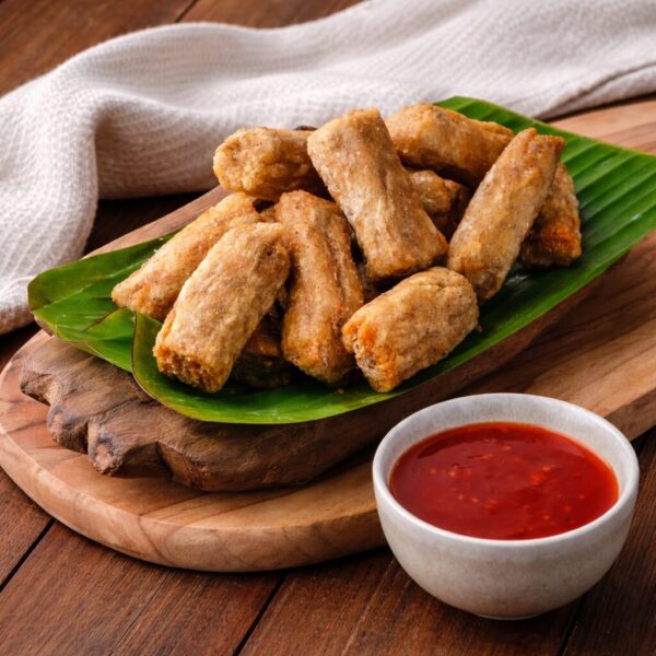 Crispy fried spring rolls served on a banana leaf with a side of red dipping sauce