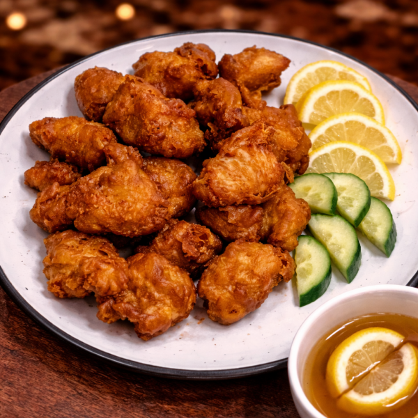 Plate of golden-brown fried chicken pieces served with cucumber slices, lemon wedges, and a side of dipping sauce