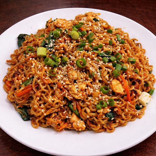 Stir-fried noodles with chicken, vegetables, and sesame seeds on a white plate