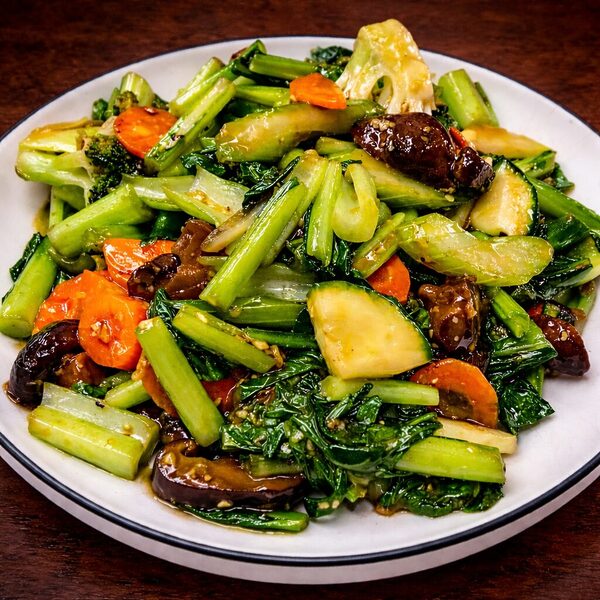 Stir-fried mixed vegetables including bok choy, carrots, broccoli, and mushrooms on a white plate
