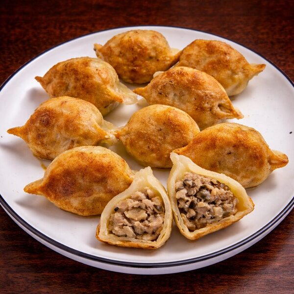 A plate of pan-fried dumplings, with one cut open to reveal a savory meat and mushroom filling