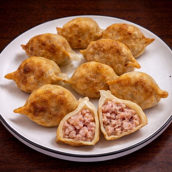 A plate of golden-brown pan-fried dumplings, with one cut in half to reveal a savory ground meat filling
