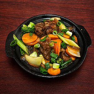 Stir-fried beef with carrots, broccoli, and green onions served in a hot cast-iron skillet