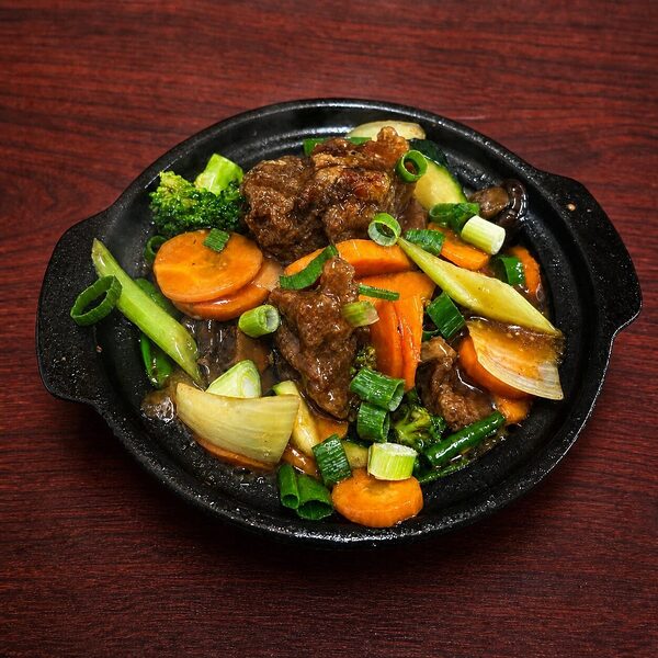 Stir-fried beef with carrots, broccoli, and green onions served in a hot cast-iron skillet