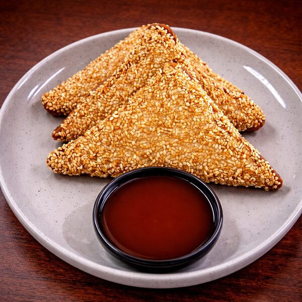 Three triangular shrimp toast pieces coated in sesame seeds, served on a plate with a side of dipping sauce