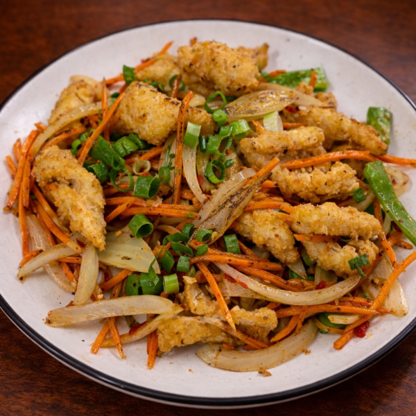 Stir-fried dish with crispy breaded chicken, sliced onions, carrots, and green onions on a white plate