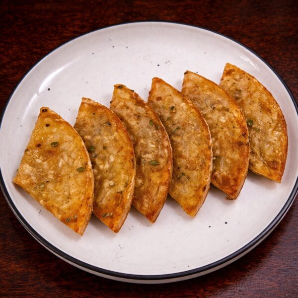 Six golden-brown, pan-fried dumplings arranged in a row on a white plate