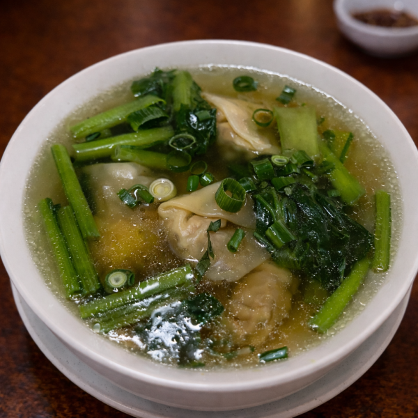 Bowl of wonton soup with leafy greens and sliced scallions in a clear broth