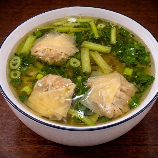 A bowl of wonton soup with three wontons and chopped green vegetables in a clear broth