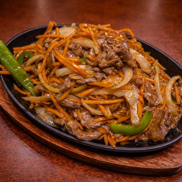Sizzling stir-fry with beef, julienned carrots, onions, and green bell peppers served on a hot cast-iron platter
