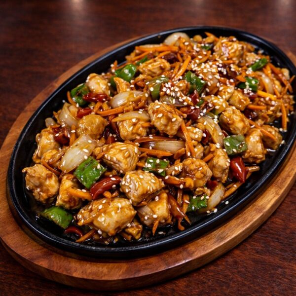 Sizzling platter of stir-fried chicken with bell peppers, onions, and carrots topped with sesame seeds