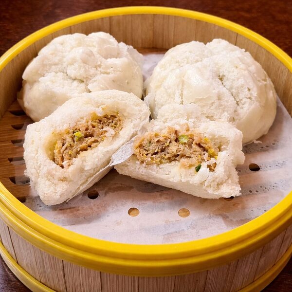 Steamed bao buns in a bamboo steamer, with one bun cut in half to reveal a savory meat filling