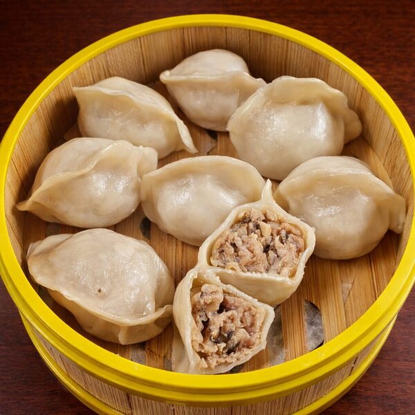 Steamed dumplings in a bamboo steamer, with one dumpling cut open to show a savory meat and mushroom filling