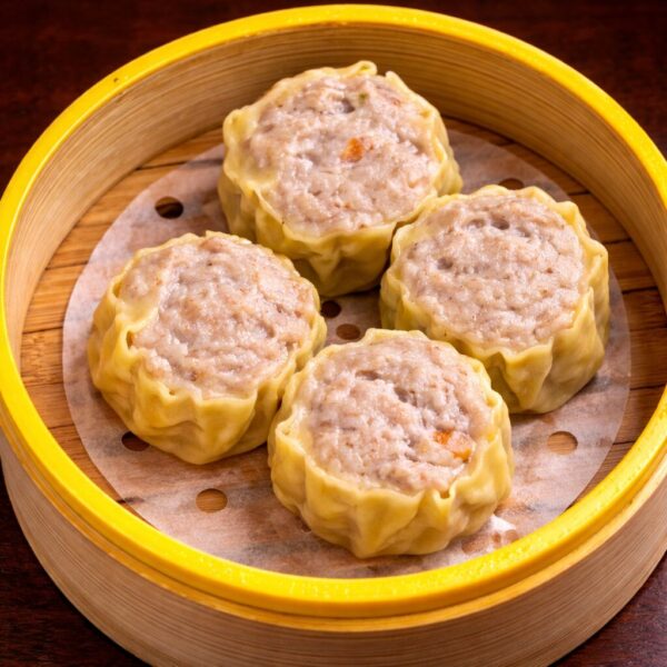 Four steamed pork siu mai dumplings served in a bamboo steamer basket