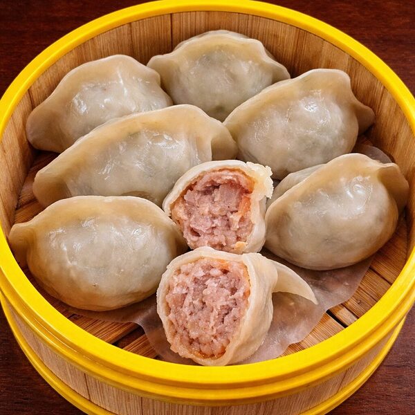 Steamed dumplings in a bamboo basket, with one dumpling cut in half to show the meat filling