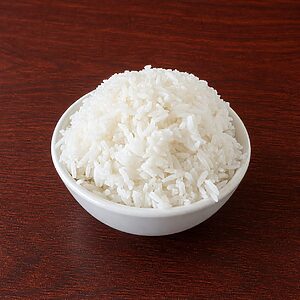 A small white bowl filled with cooked white rice on a dark wooden surface