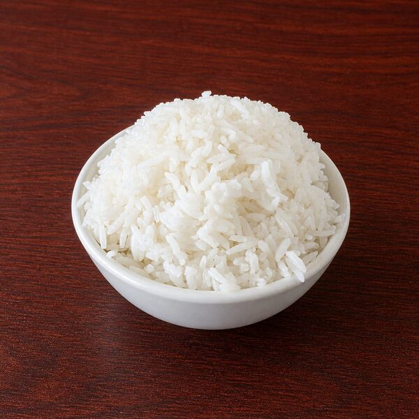 A small white bowl filled with cooked white rice on a dark wooden surface