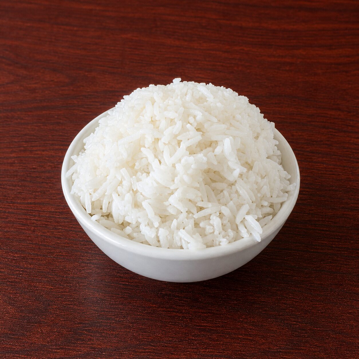 A small white bowl filled with cooked white rice on a dark wooden surface