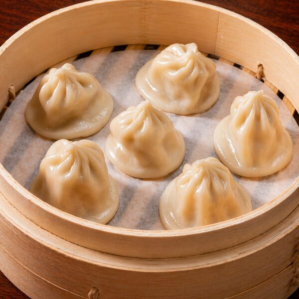 Six steamed soup dumplings served in a bamboo steamer basket