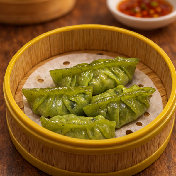 Four vibrant green vegetable dumplings served in a bamboo steamer basket with a side of dipping sauce