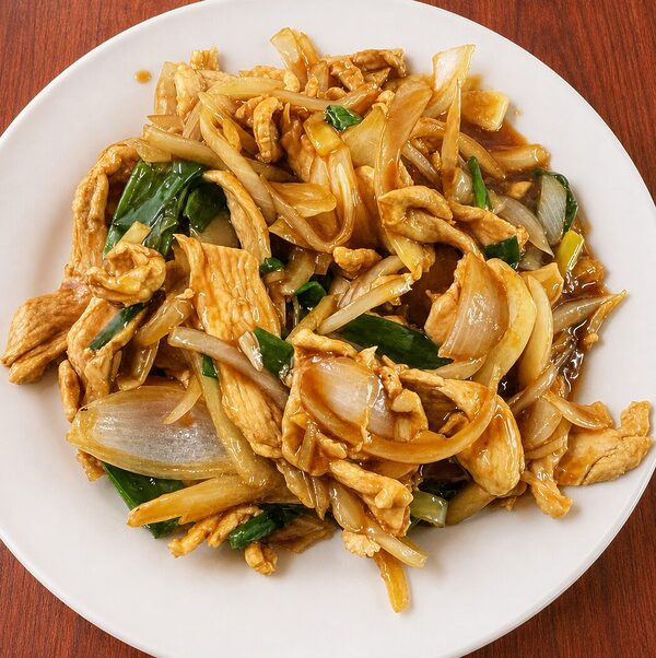 Stir-fried chicken with onions and green scallions in a savory brown sauce on a white plate