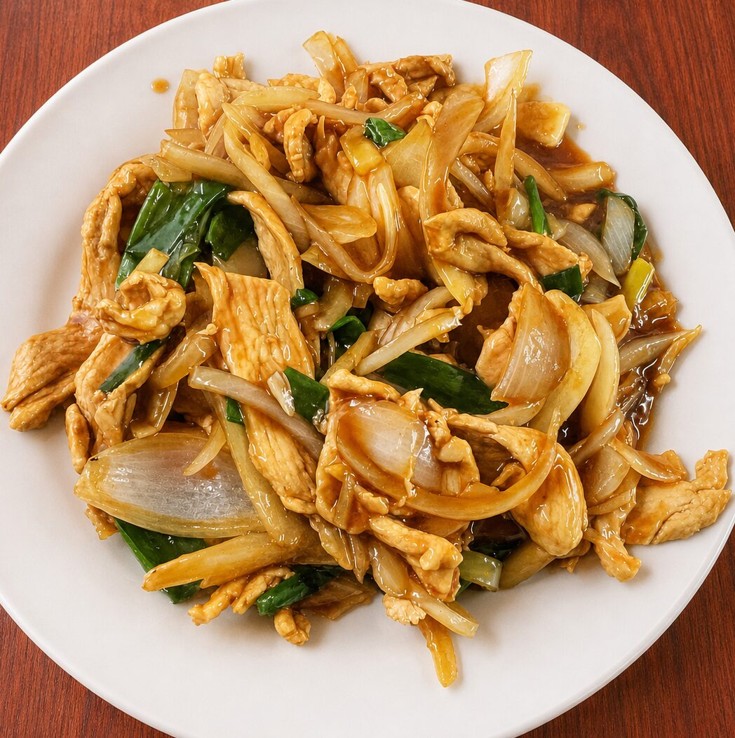 Stir-fried chicken with onions and green scallions in a savory brown sauce on a white plate