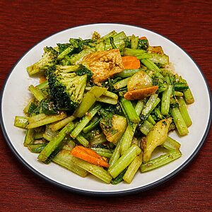 Stir-fried dish of broccoli, leafy greens, carrots, and tofu on a white plate
