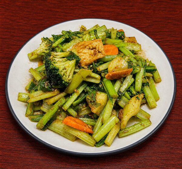 Stir-fried dish of broccoli, leafy greens, carrots, and tofu on a white plate