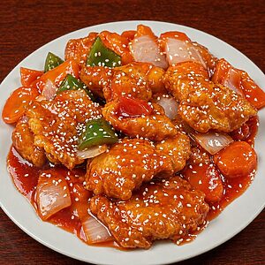 Sweet and sour chicken with bell peppers, onions, and carrots, sprinkled with sesame seeds on a white plate