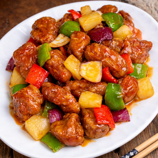 Sweet and sour pork with pineapple, red and green bell peppers, and red onion on a white plate