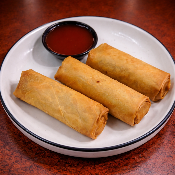 Three golden-brown fried spring rolls served on a white plate with a side of red dipping sauce